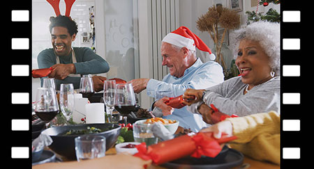 Diverse multi generation family pulling Christmas crackers as they sit for meal at table
